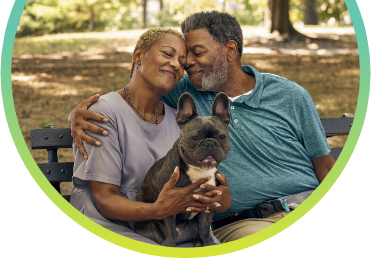 A man and a woman sitting on a park bench with a dog in their lap.